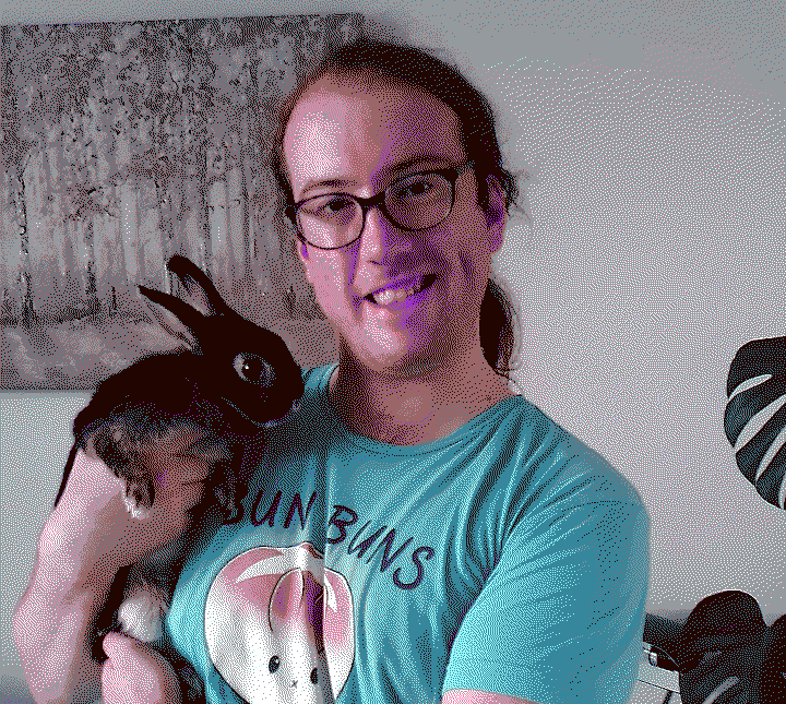 A person with glasses and ponytail, wearing a blue bun buns shirt, holding a black bunny and smiling to the camera