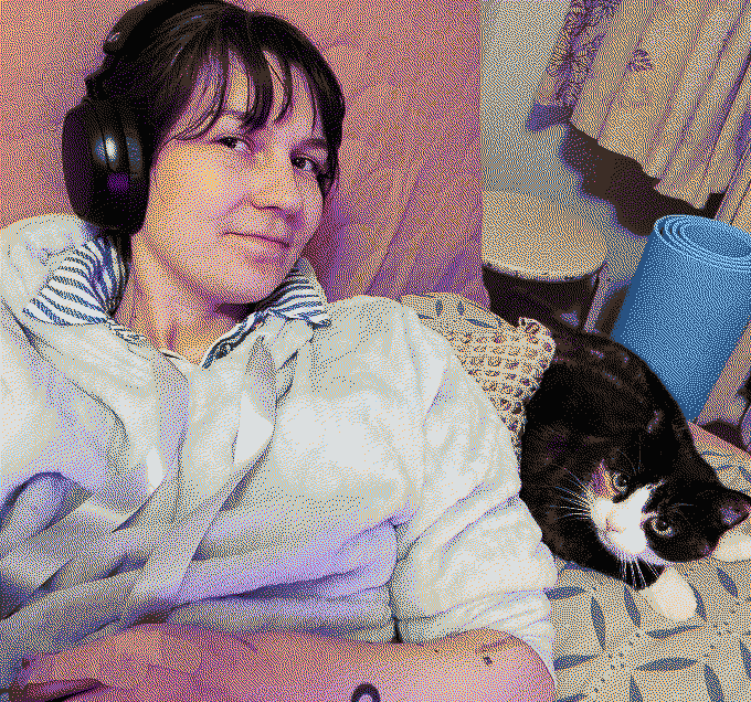 A girl with headphones and a 3-colour cat with white paws and nose relaxing on a yellow couch